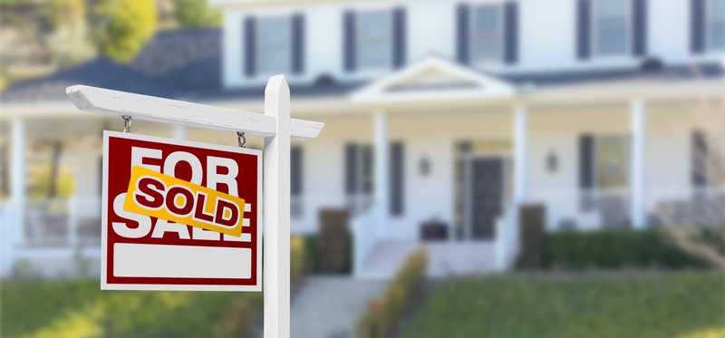 A home in the background with for sale/sold sign in foreground.