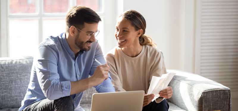 Two people smile at each other while reviewing paperwork in front of laptop.