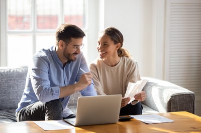 Two people smile at each other while reviewing paperwork in front of laptop.