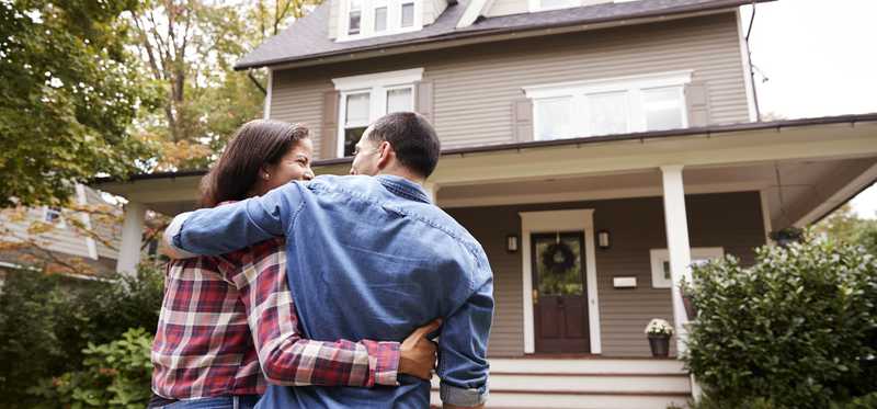 A couple hugs one another in front of a house.