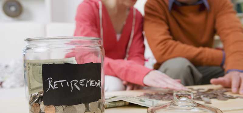 Retirement jar full of coins in the foreground and young couple in the background.