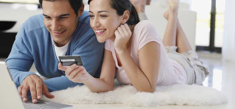 Young couple shopping with credit card in hand on a laptop.