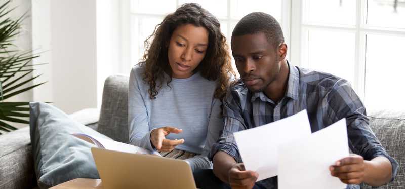 Two people talk about paperwork in front of laptop.
