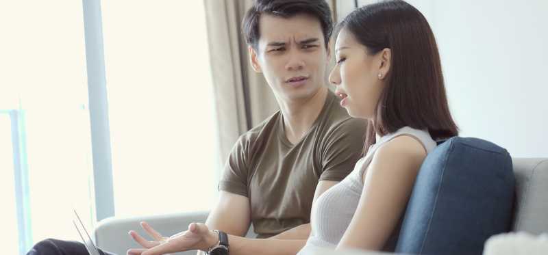 Two people talking while one looks at laptop.