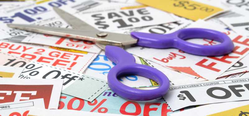 A pair of scissors lying on top of a messy pile of coupons.