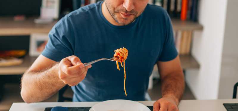 A man eats spaghetti alone at a table.