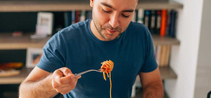 A person eats spaghetti alone at a table.