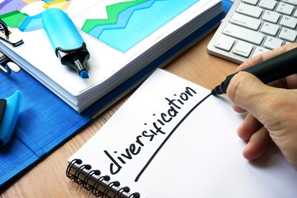 Person writing the word Diversification on a notepad in black marker.
