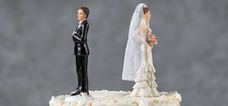 Wedding couple figurines on a wedding cake facing away from each other.