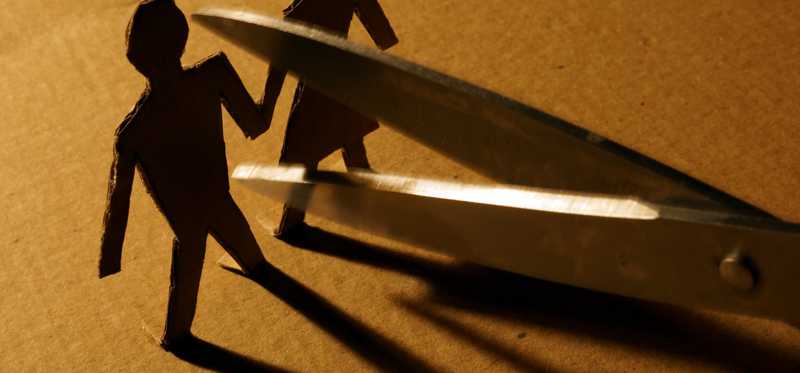 A paper man and woman are being cut in half by a pair of scissors.