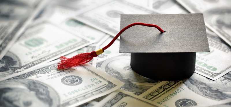 Graduation cap on a spread out pile of $100 bills.