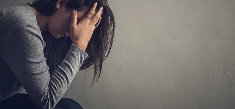 Person in dark lighting with hands to face in emotion.