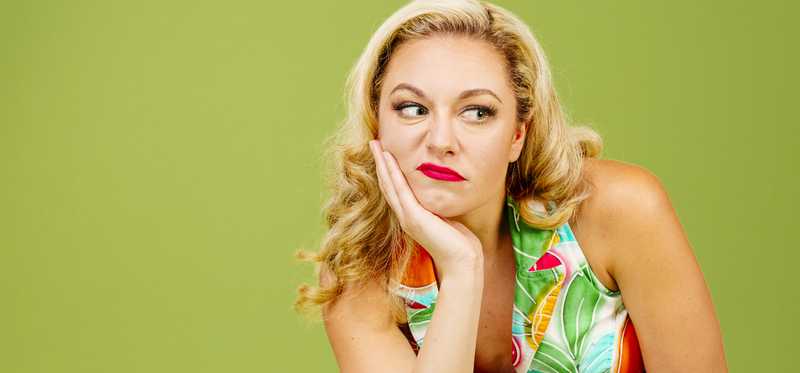 Blonde woman with hand on chin looking dismayed in front of green background.