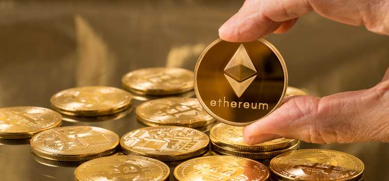 A pile of gold coins and a hand holding up one that says Ethereum.