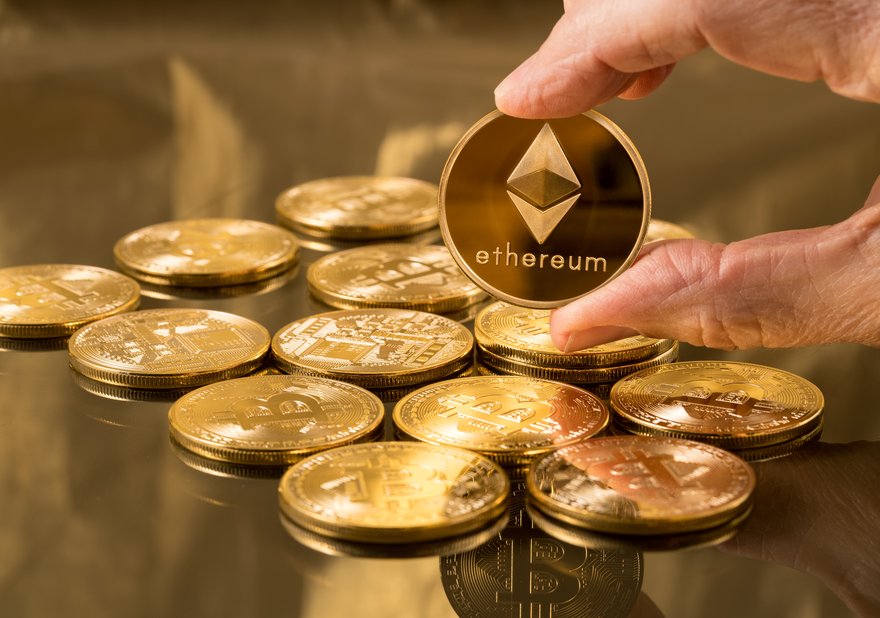 A pile of gold coins and a hand holding one up that says Ethereum.