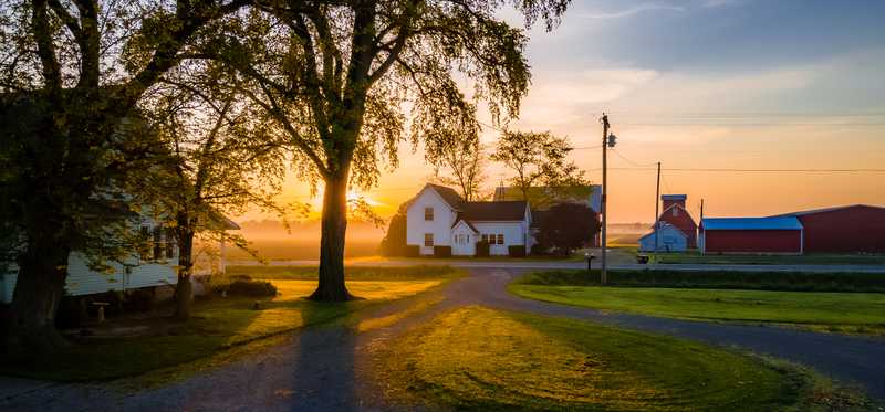 A farmhouse in the distance on a large piece of property.