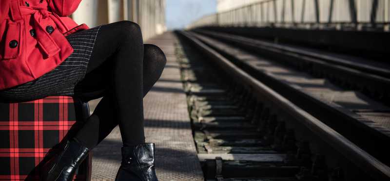 A girl sitting on a bridge wearing a red coat, black skirt, and black booties