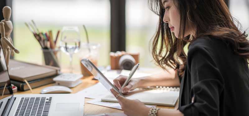Designer looking at a tablet while writing a note.