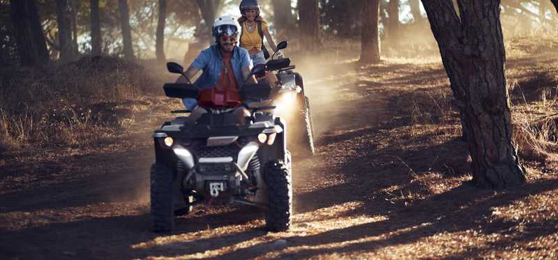 Two people riding four-wheelers in a path through the woods.