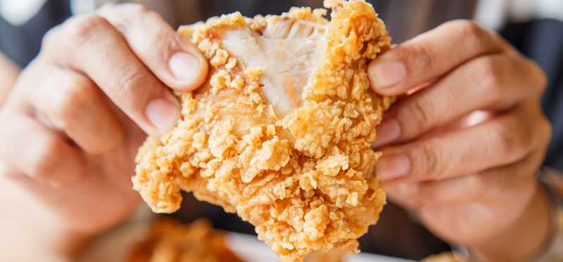 A piece of fried chicken is held up.