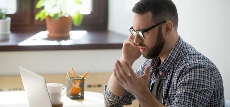 Frustrated person on phone at laptop.