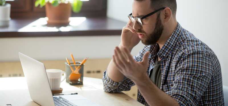 Frustrated man on phone at laptop.