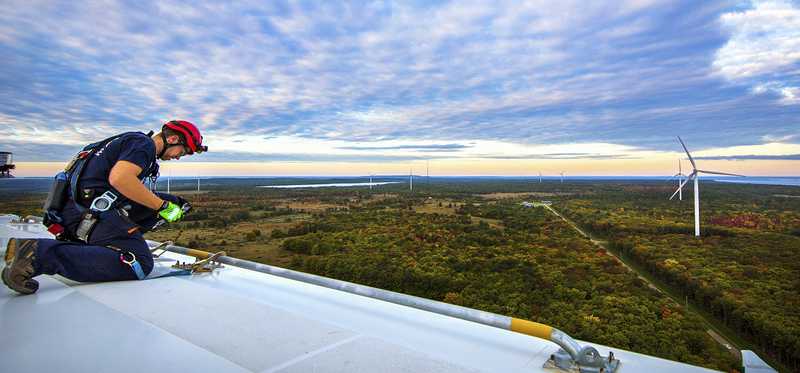 A technician working on a roof with windmills in the background.