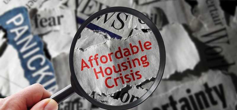 Hands holding a magnifying glass over a slip of newspaper that says Affordable Housing.