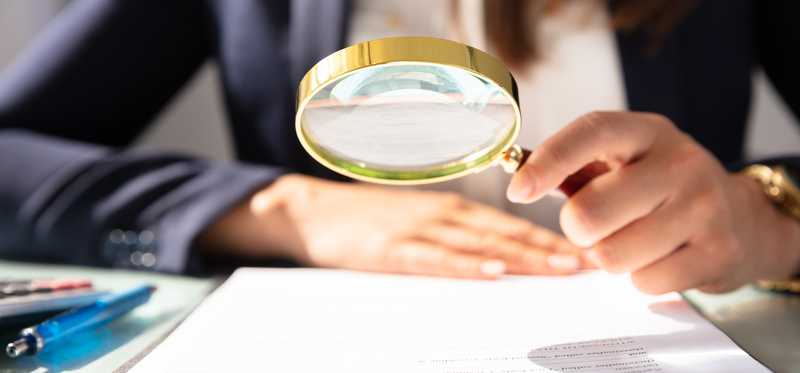 Person looking at document through magnifying glass.