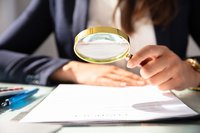 Person looking at document through magnifying glass.