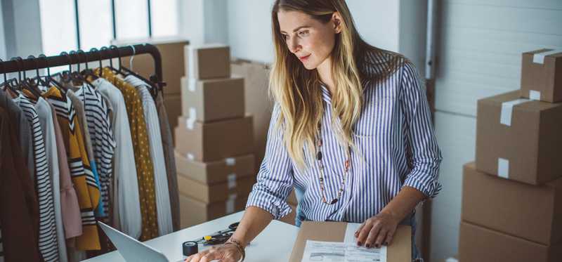 Person using laptop and preparing small box for shipping.