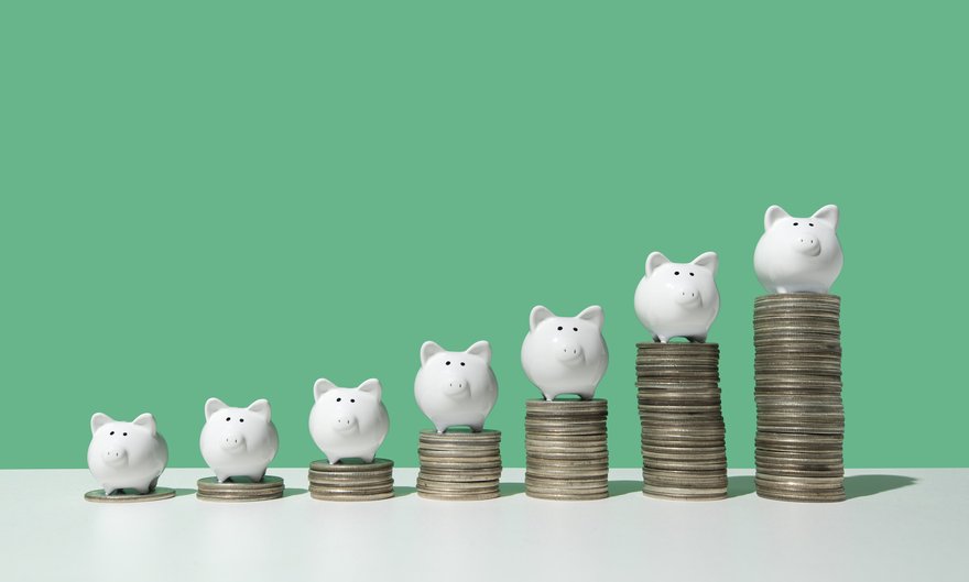 Little white piggy banks standing on top of seven stacks of coins in ascending order.