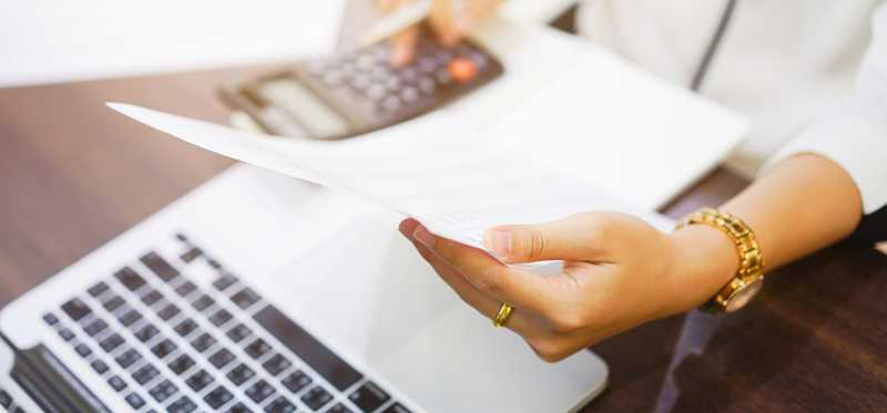 Person holding a report and using a calculator at a desk.