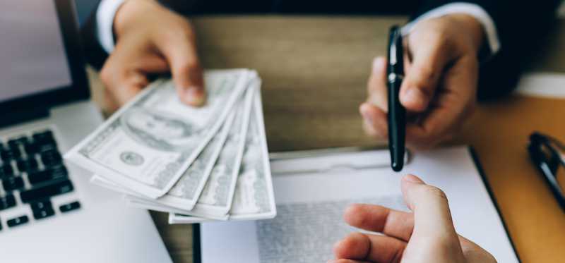 Person passing cash and a pen over a contract or agreement.