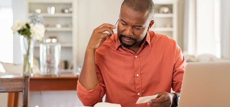 Person on phone looking at books and receipts in front of laptop.