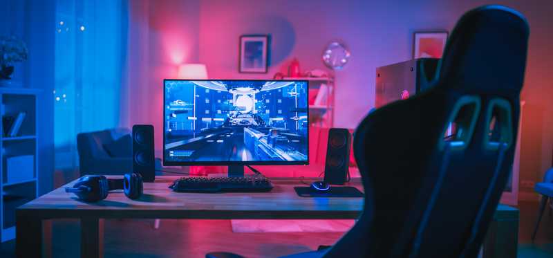 Empty chair in front of computer desk with virtual game playing on computer screen.