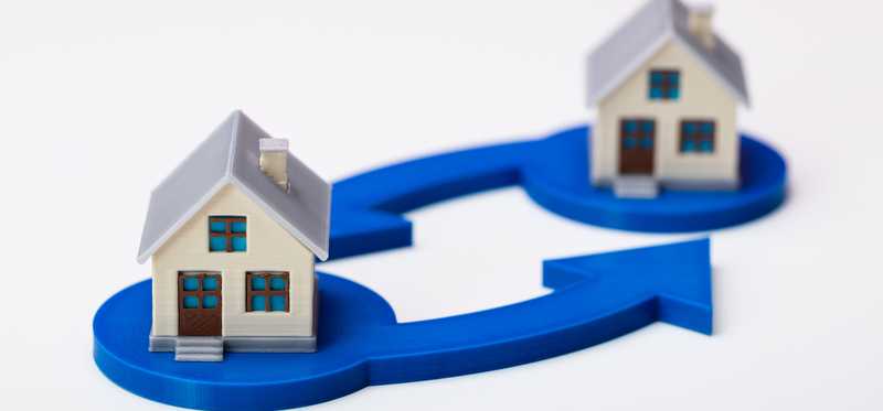 Two model houses sitting atop blue arrows pointing in a circular exchange motion.