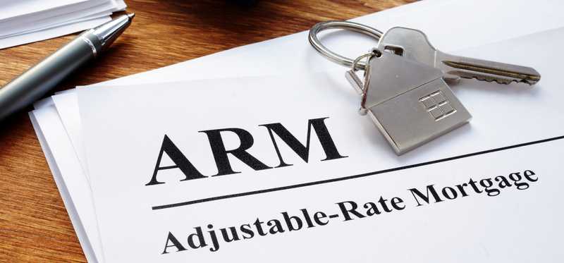 Adjustable-rate mortgage paperwork lying on a desk next to house a key.