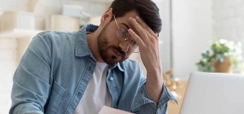 Worried person with their hand on their forehead looking at documents.