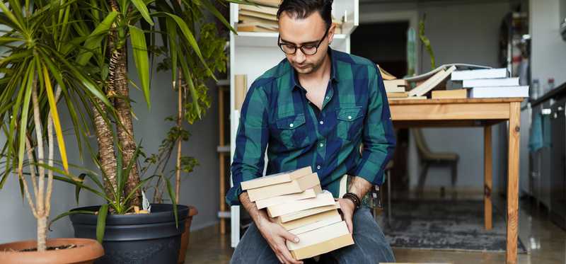 Person cleaning off and decluttering bookshelf.