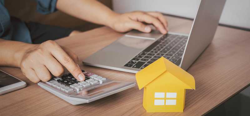 Person using a laptop and calculator to research mortgage loans.