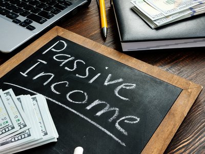 Passive Income written on a chalkboard with money lying on top.
