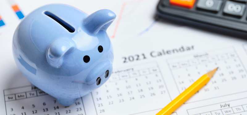 A piggy bank and calculator sitting on a calendar.