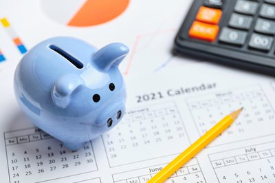 A piggy bank and calculator sitting on a calendar.