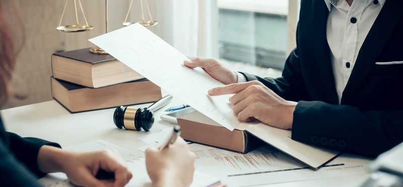 Two people talking and reading paperwork at desk with legal books and gavel.