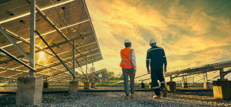 Two people walking near solar energy panels with a sunset in the background.