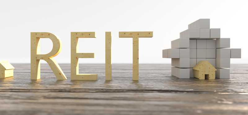 Wooden blocks spelling REIT next to real estate building blocks.