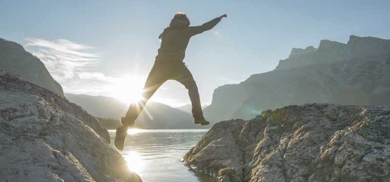 Person jumping from one bank of a lake to another.
