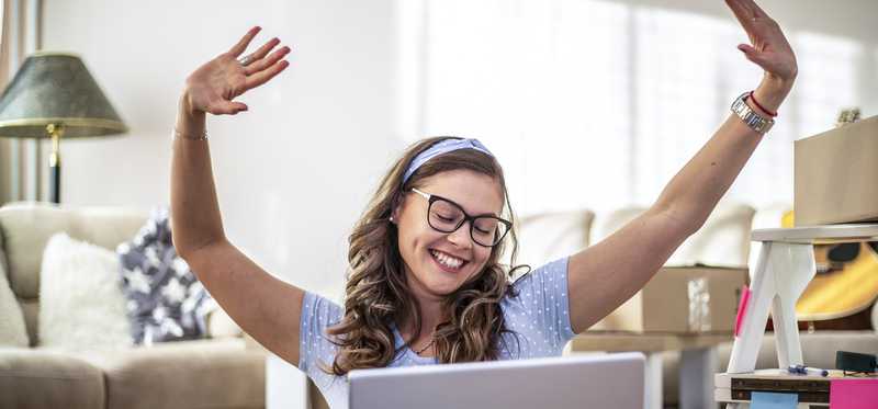 Person in front of computer is excited and smiling with hands in air.