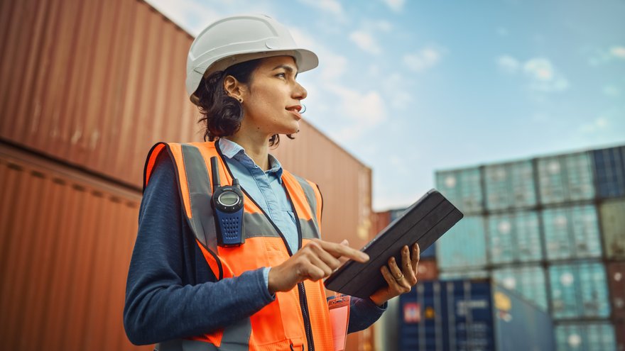 Person in hard hat using a tablet to locate something in a shipping yard.